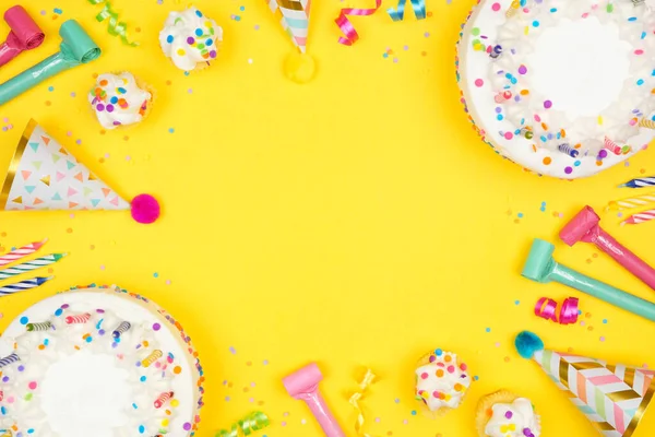 Birthday party frame on a yellow background. Overhead view with cakes, party hats and confetti. Copy space.