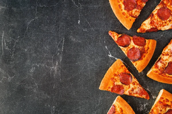 Pepperoni pizza slice side border. Above view over a dark slate background. Copy space.