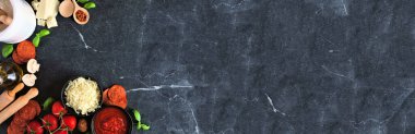Pizza making ingredients including cheese, pepperoni, tomatoes and basil. Above view corner border against a dark banner background. Copy space.