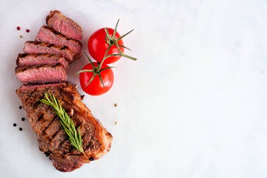 Delicious grilled steak sliced. Top view on a white marble background with copy space.