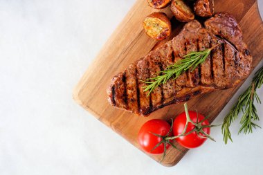 Juicy grilled steak on a serving board. Top view on a white marble background.