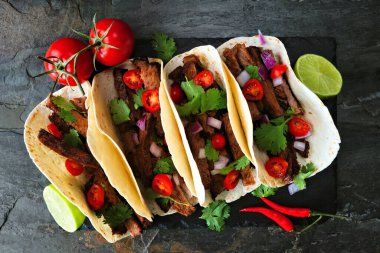 Tacos with steak, tomatoes, onion and cilantro. Above view on a dark background.
