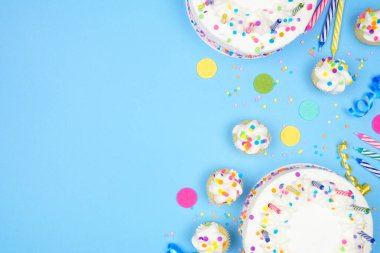 Birthday party side border on a blue background. Top view with cakes, party hats and confetti. Copy space.