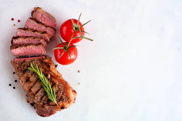 Delicious grilled steak sliced. Top view on a white marble background with copy space.
