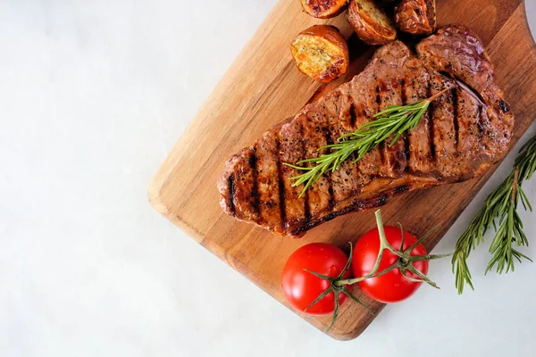 Juicy grilled steak on a serving board. Top view on a white marble background.