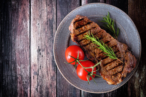 Juicy grilled steak on a plate. Top down view on a dark wood table background.
