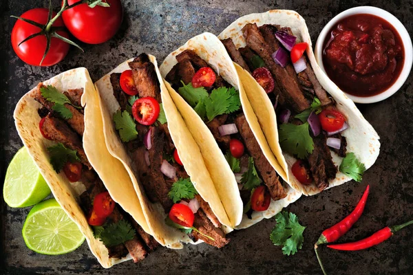 Mexican tacos with steak, tomatoes, onion and cilantro. Top on a dark background.