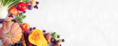 Fall food corner border with pumpkins, apples, squash and a variety of vegetables. Top view on a white marble banner background with copy space.