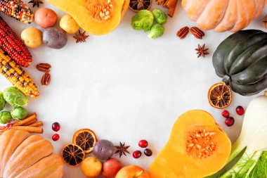 Fall food frame with pumpkins, apples, squash and a collection of vegetables. Above view on a white marble background with copy space.