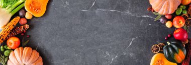 Autumn food double border with pumpkins, apples, squash and a variety of vegetables. Overhead view on a dark stone banner background with copy space.