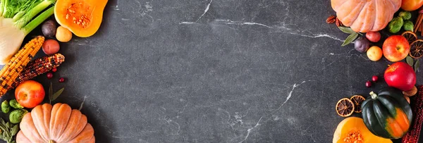 Autumn food double border with pumpkins, apples, squash and a variety of vegetables. Overhead view on a dark stone banner background with copy space.