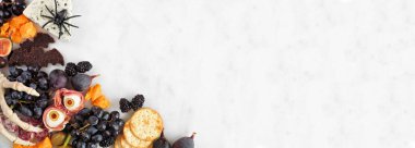 Halloween theme charcuterie corner border against a white marble background. Assorted cheeses and meat appetizers. Copy space.