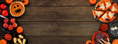 Fun Halloween dinner party double border over a dark wood banner background. Top down view. Pizza, jack o lantern pumpkin pie, candy apples, eyeball spaghetti, snacks and spooky punch.