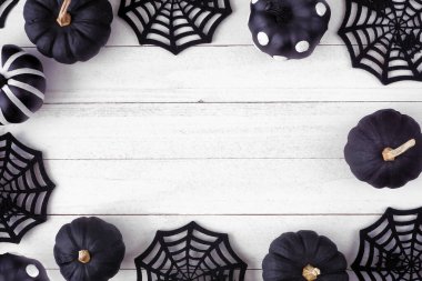 Halloween frame of black and white patterned pumpkins and spider web decor. Top view on a white wood background. Copy space.