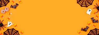 Halloween double border of scattered candy and decor. Top view over an orange banner background with copy space.
