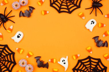 Halloween frame of scattered candy and decor. Top down view over an orange background with copy space.