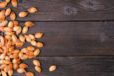 Autumn pumpkins seeds, salted and roasted. Top down view side border over a dark rustic wood background. Halloween treat. Copy space.