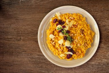 Autumn pumpkin risotto with cranberries and parmesan cheese. Top down view on a rustic wood background.