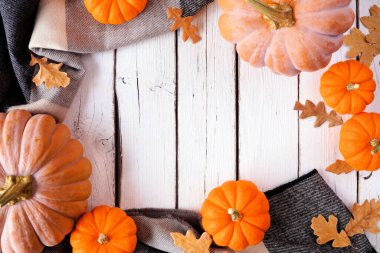 Cozy fall frame with pumpkins, leaves and blanket. Top view over a white wood background.