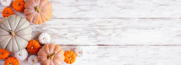 Fall corner border of pumpkins of various sizes and colors over a rustic white wood banner background. Above view with copy space.