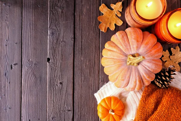 Cozy fall side border with pumpkins, sweaters and candles. Overhead view over a dark wood background.
