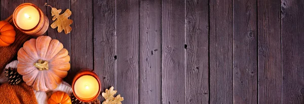 Cozy fall corner border with pumpkins, sweaters and candles. Top down view over a dark wood banner background.