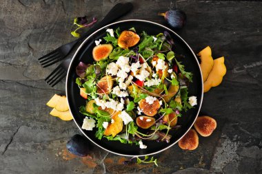 Sonbahar salatası, kızarmış kabak, elma, incir ve siyah tabakta beyaz peynir. Malzeme çerçevesi ile koyu bir arkaplan üzerinde görünüm.