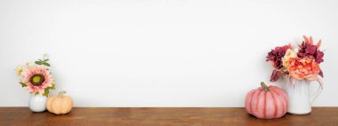 Ahşap bir rafta beyaz bir duvar pankartıyla dekor oluşturun. Pembe renkte balkabakları ve çiçekler sonbahar renkleri. Boşluğu kopyala.