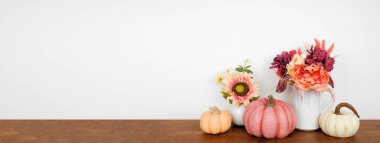 Ahşap bir rafta, arka planda beyaz bir duvar pankartıyla sonbahar dekoru. Pembe renkte balkabakları ve çiçekler sonbahar renkleri. Boşluğu kopyala.