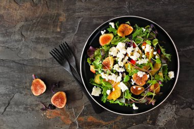 Sonbahar salatası, kızarmış kabak, elma, incir ve siyah tabakta beyaz peynir. Koyu bir arkaplanda tepeden aşağı görünüm.
