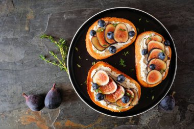 İncirli, krem peynirli ve yabanmersinli Crostini aperatifleri. Koyu bir arkaplanda genel görünüm.