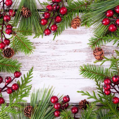 Her zaman yeşil dalları, kırmızı böğürtlenleri ve çam kozalakları olan bir Noel çerçevesi. Kopya alanı olan bir köy kare beyaz ahşap zemin üzerinde görünüm.
