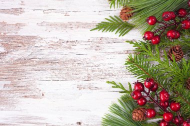 Her zaman yeşil dalları, kırmızı böğürtlenleri ve kozalakları olan kış kenarı sınırı. Kopyalama alanı olan kırsal beyaz ahşap arkaplan üzerindeki üst görünüm.