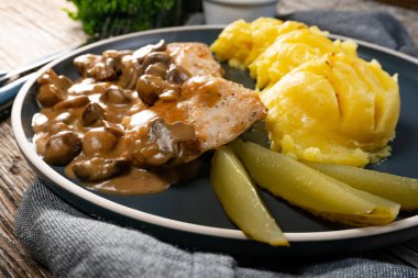 Mantar soslu ızgara tavuk göğsü, patates püresi ve salatalık turşusu ile servis edilir..