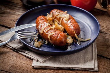 Kızarmış sosis bir tabak içinde soğan ile.