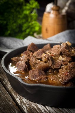 Dökme demir tavada sığır güveci, ahşap arka plan. Sığ alan derinliği.