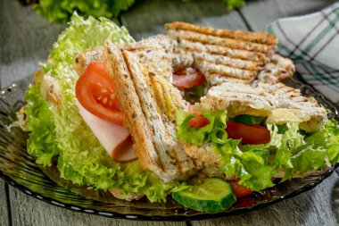 Panini sandviçle jambon, domates, marul bir plaka üzerinde.