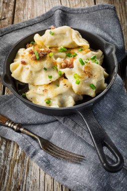 Fırında hamur köftesi (pierogi), içinde dökme demir tavada yeşillikler serpiştirilmiş..