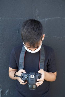 Yeşil gözlü, maske takan küçük şirin bir çocuk elinde bir kamera tutuyor ve fotoğraf çekiyor. Mutlu çocuk fotoğrafçı olmayı hayal ediyor..