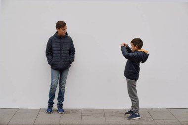 Beyaz beton duvarın önünde poz veren şık bir çocuk. Çocuklar için tarz ve moda kavramı.