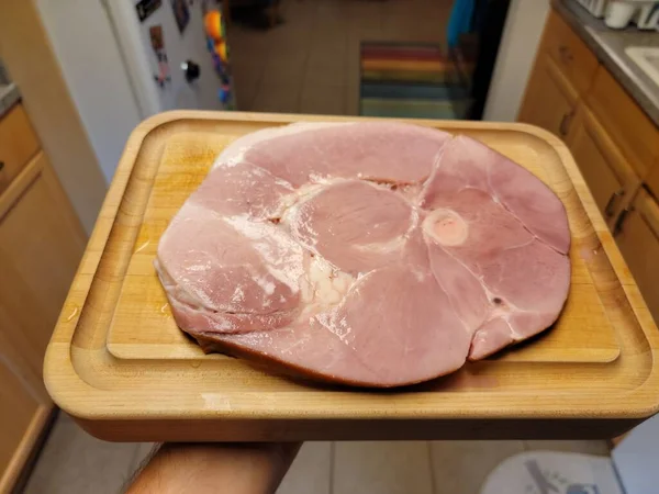 Main tenant grande tranche de jambon sur planche à découper en bois — Photo