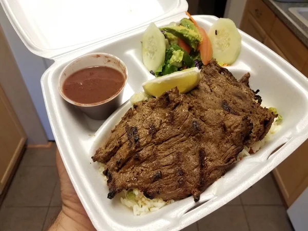 beef steak meat with vegetables in take out container held in kitchen