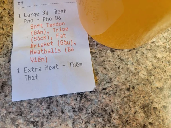 Vietnamese pho soup broth with receipt saying extra meat on counter