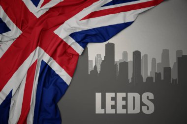 Şehrin soyut silueti. Üzerinde yazı var. Büyük Britanya bayrağının gri arka planda dalgalanması yakınındaki Leeds yazıları..