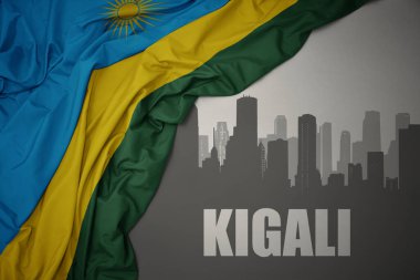 abstract silhouette of the city with text Kigali near waving colorful national flag of rwanda on a gray background. 3D illustration