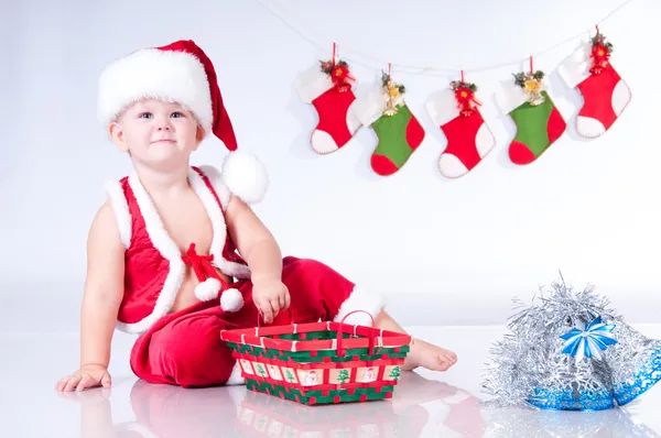 Cute baby Santa Claus with garlands and Christmas basket — Stock Photo, Image