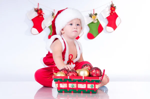 Cute baby Santa Claus with garlands and a basket of Christmas to — Stock Photo, Image