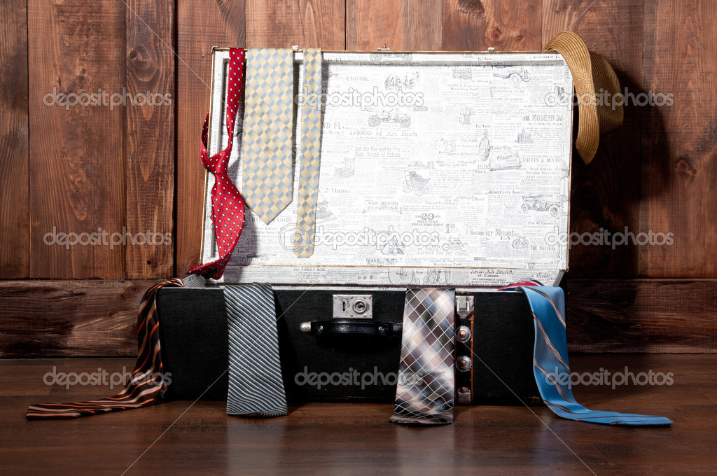Vintage suitcase with a tie, against a wooden wall.