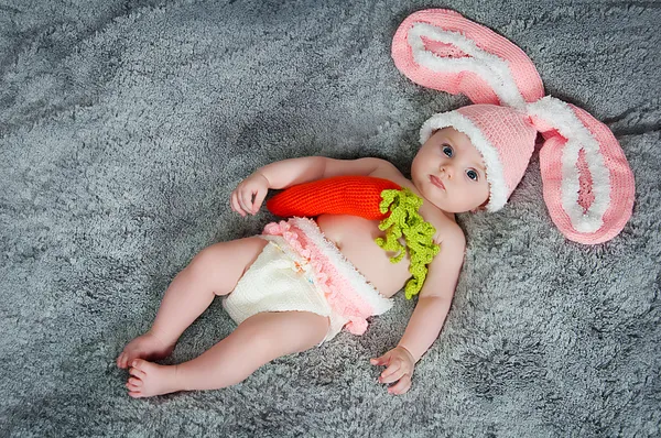 Petit enfant avec des oreilles de lapin. Allongé sur le dos avec des carottes . — Photo