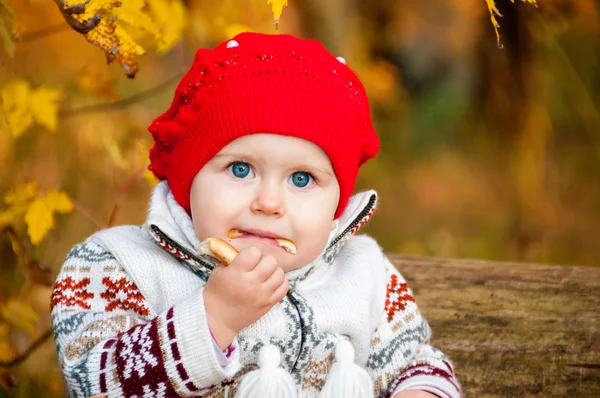 Ormanda oturan ve bir simit yiyen sevimli küçük bebek kız — Stok fotoğraf